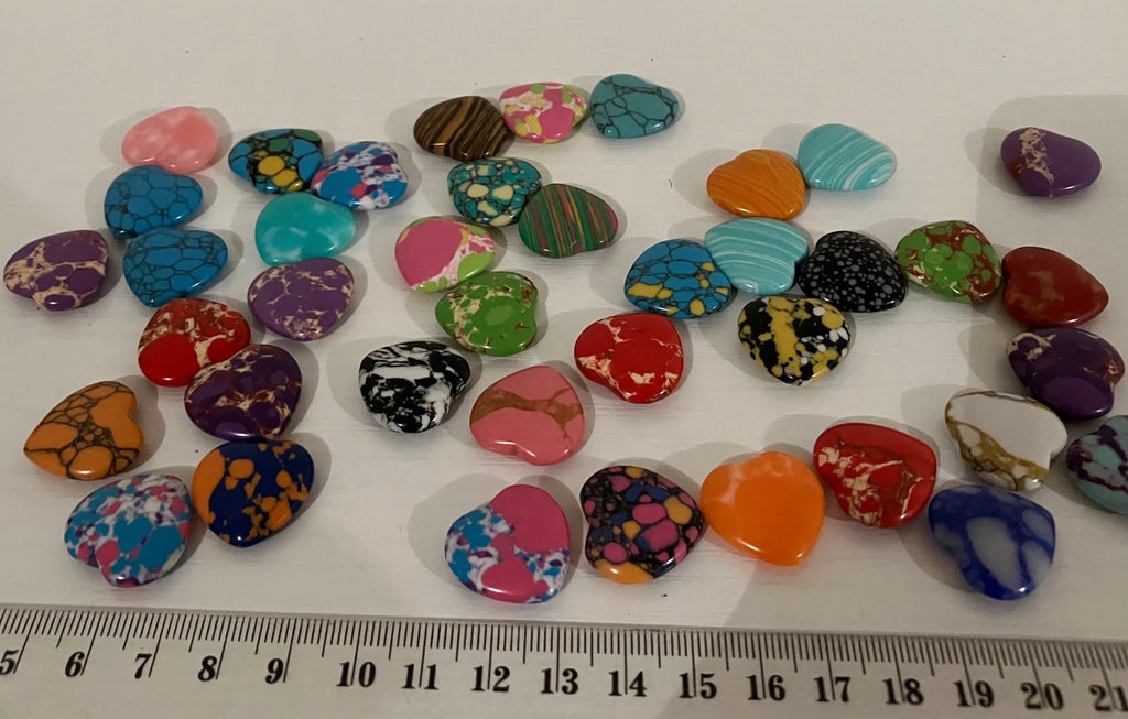 A collection of small, irregularly shaped craft stones or beads in various colorful marbled and speckled patterns, arranged on a white surface with a ruler at the bottom for scale.