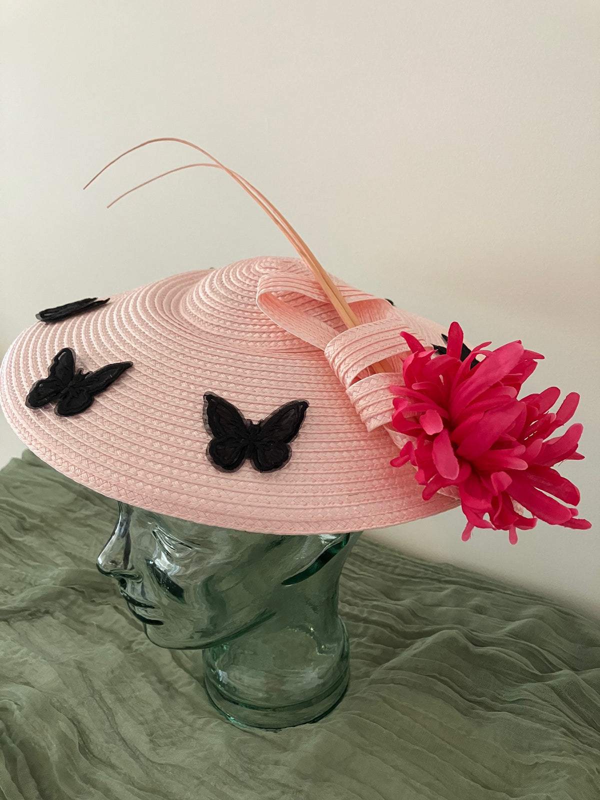 Ladies light pink woven fascinator hat with black butterfly appliqués and a bright pink feather flower
