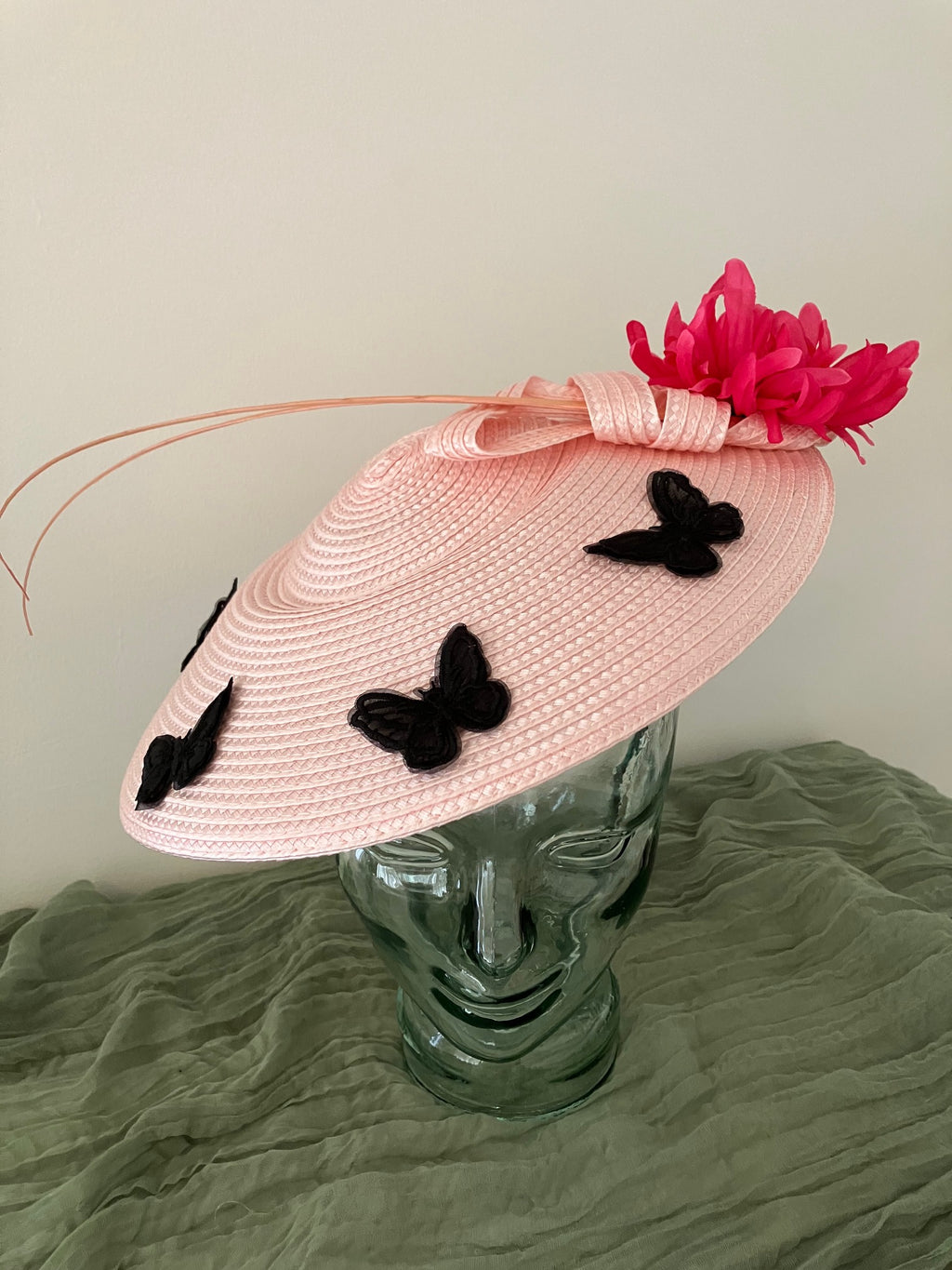 Ladies light pink woven fascinator hat with black butterfly appliqués and a bright pink feather flower