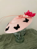 Ladies light pink woven fascinator hat with black butterfly appliqués and a bright pink feather flower