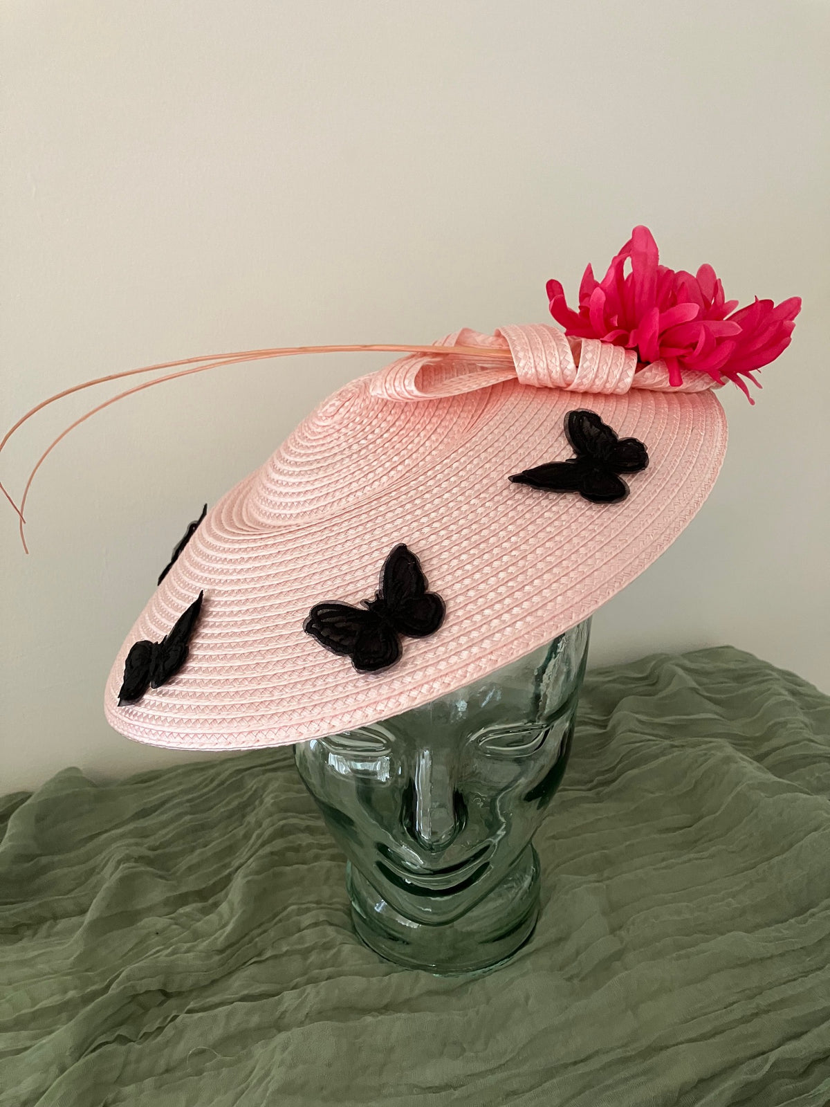 Ladies light pink woven fascinator hat with black butterfly appliqués and a bright pink feather flower