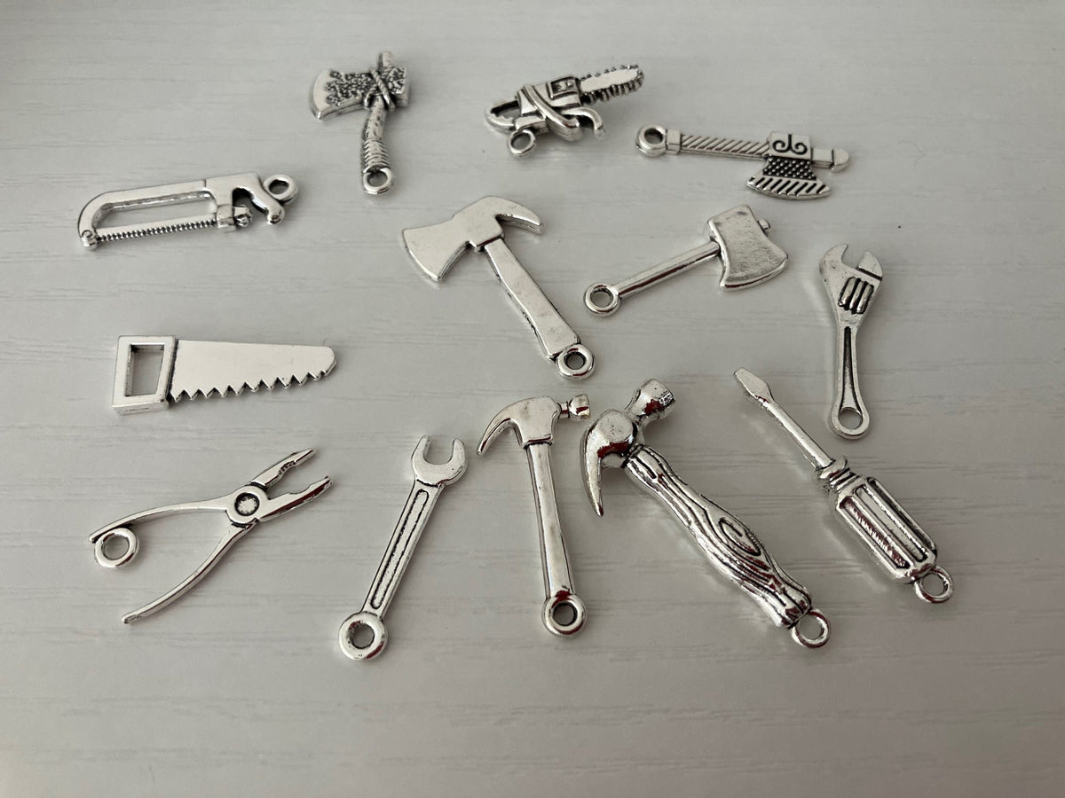 A set of silver-colored metal jewelry charms shaped like various hand tools, including pliers, saws, wrenches, hammers, axes, and screws.