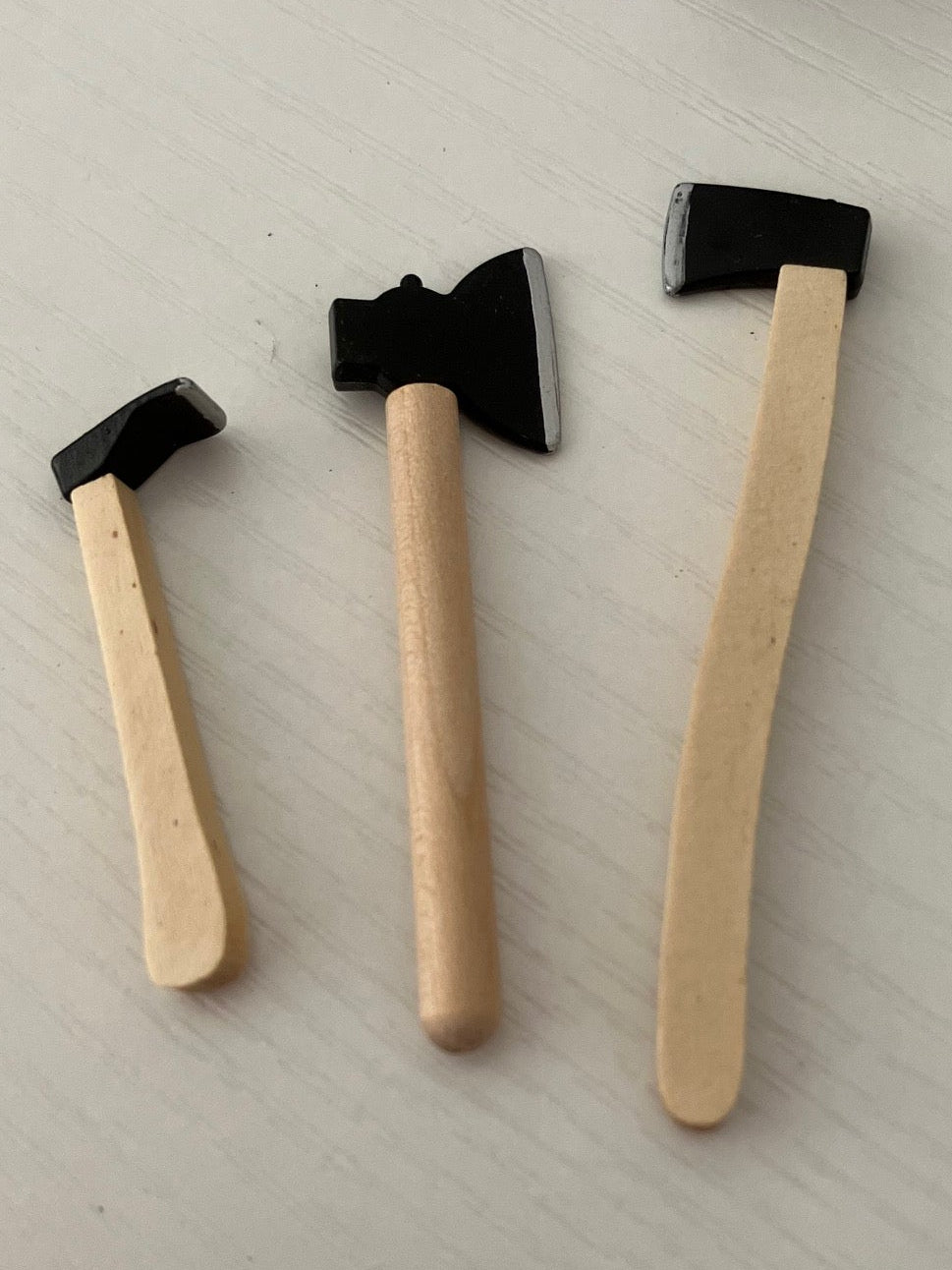 Three miniature toy axes with light wood handles and black heads.