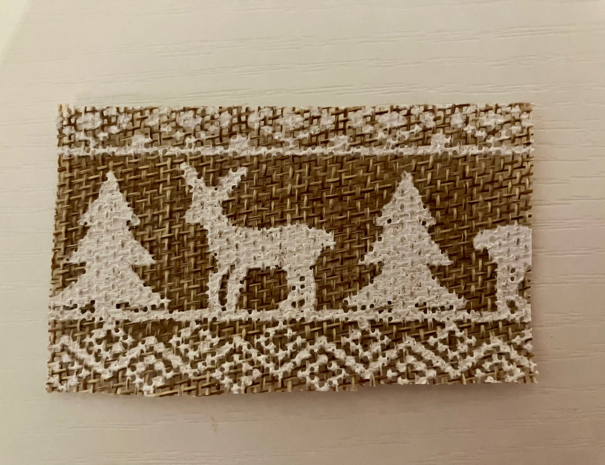 A rectangular woven decorative mat featuring a rustic holiday design with a reindeer, Christmas trees, and snowflake patterns in natural brown and cream on a light background.