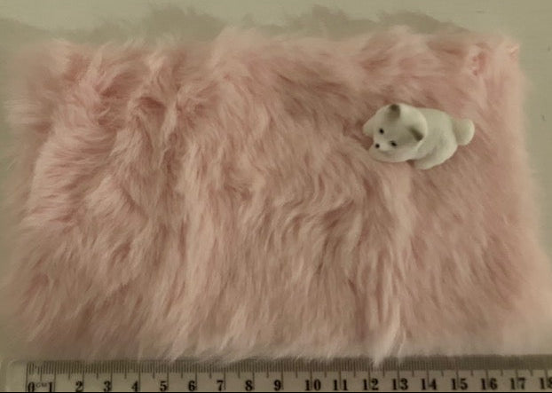 A fluffy pink faux fur blanket or cushion with a small white cat figurine resting on top, shown against a plain light background with a ruler at the bottom for scale.