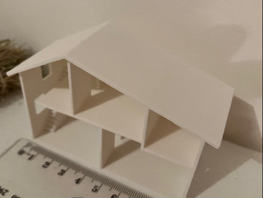 A small white 3D-printed house model shown next to a ruler for scale.