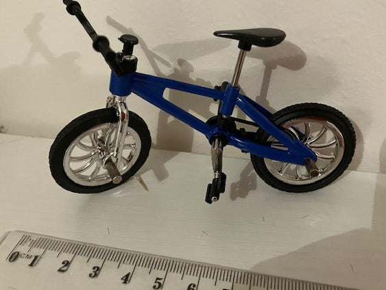 A miniature blue bicycle with black tires and silver rims, shown next to a ruler for scale.