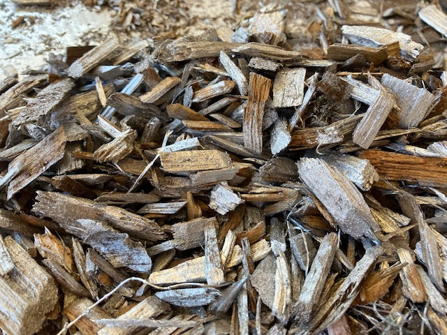 A close-up pile of natural wood chips and bark mulch pieces in varying shades of brown and tan.